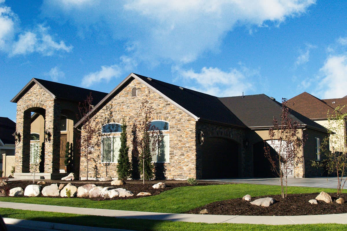 House plan exterior: Two-story home with stone facade, arched entryway, and attached garage. Gable rooflines with dormers are visible.