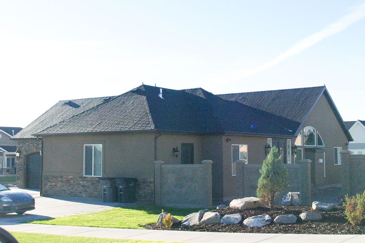 House plan exterior: One-story home with dark asphalt shingle roof, stone accents on garage, and arched window entry.