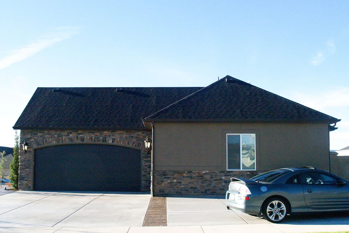 House plan exterior: One-story dwelling with arched garage, stone accents, and dark shingle roof.