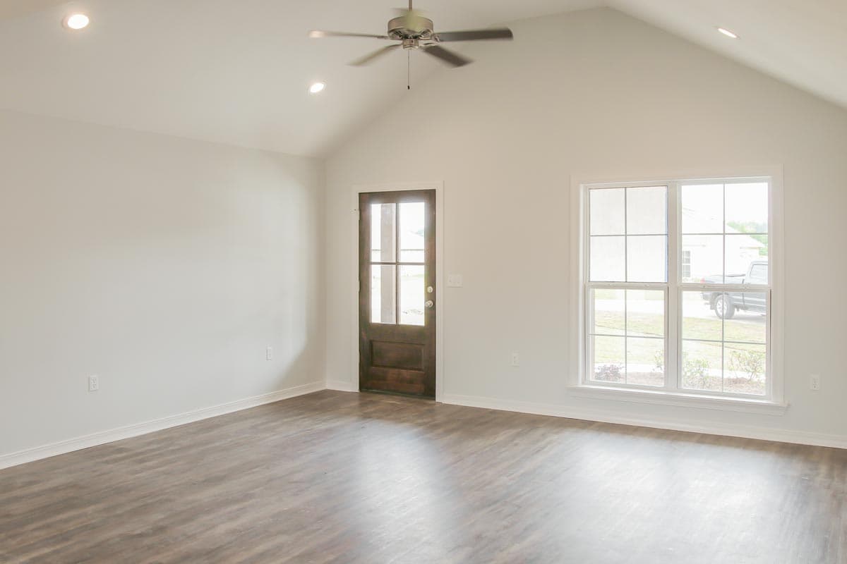 Interior view of living space with vaulted ceiling, ceiling fan, wood-paneled door, and large window.