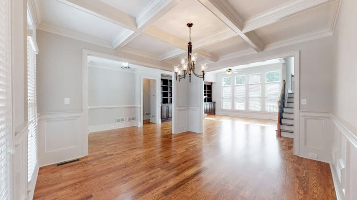 Interior view of a home with a coffered ceiling, hardwood floors, and a staircase leading to the upper level.