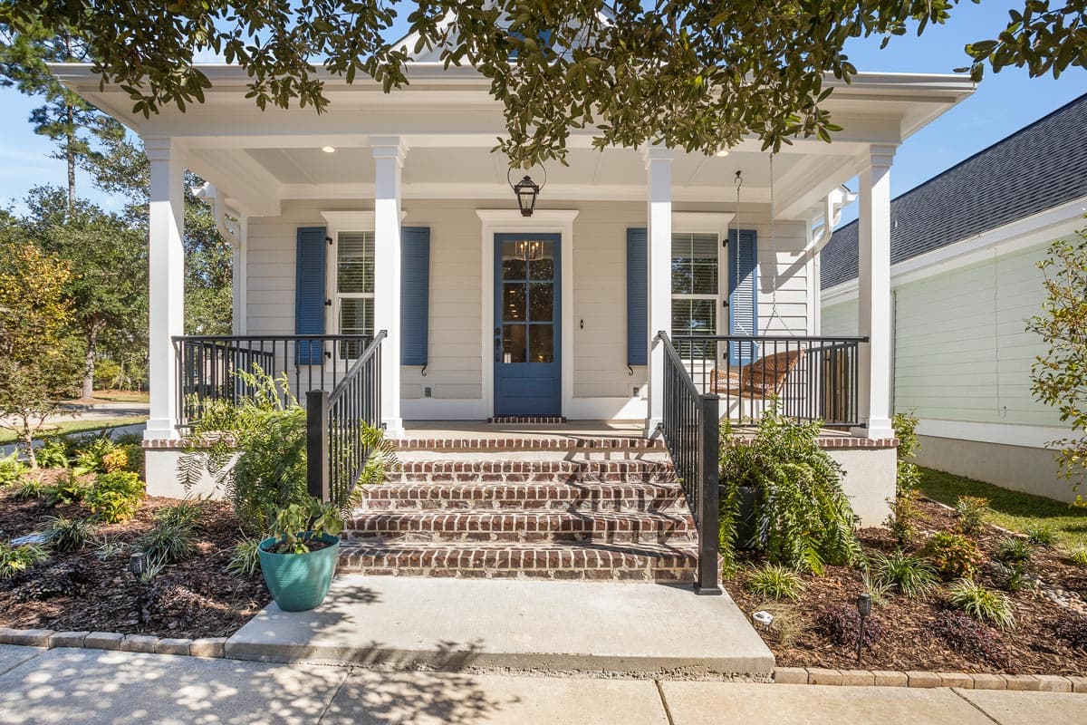 House plan exterior with a covered front porch, brick steps, white columns, and blue shutters.