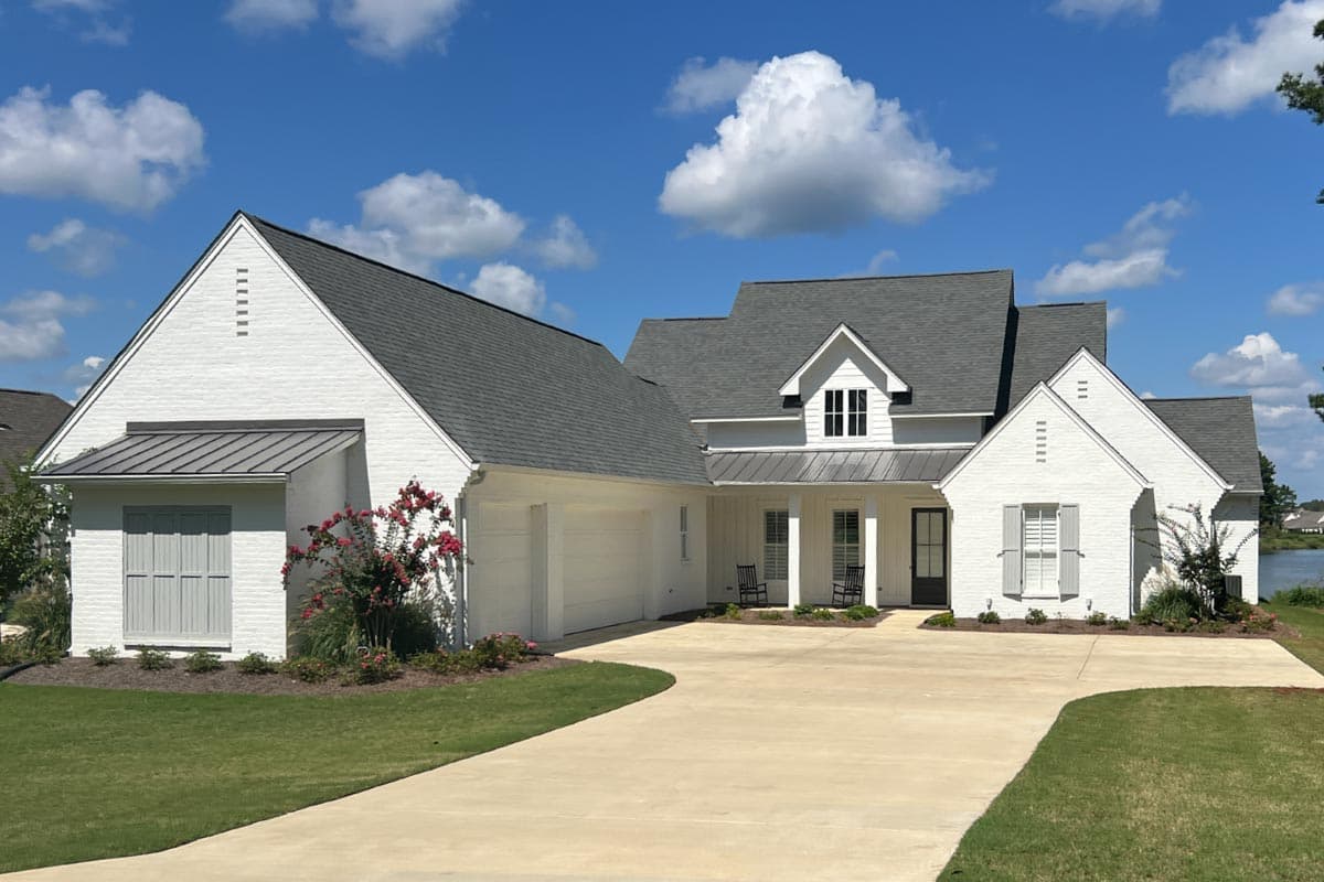 House plan exterior with white brick facade, gabled rooflines, a front porch, and a two-car garage. Features include decorative shutters.
