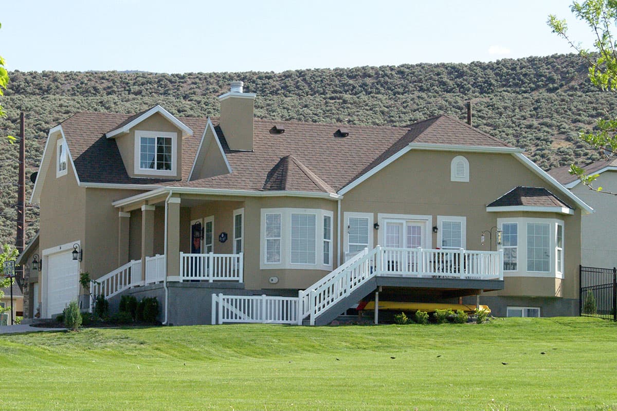 House plan exterior with two stories, a front porch with columns, a gable roof, multiple dormers, and a two-car garage.
