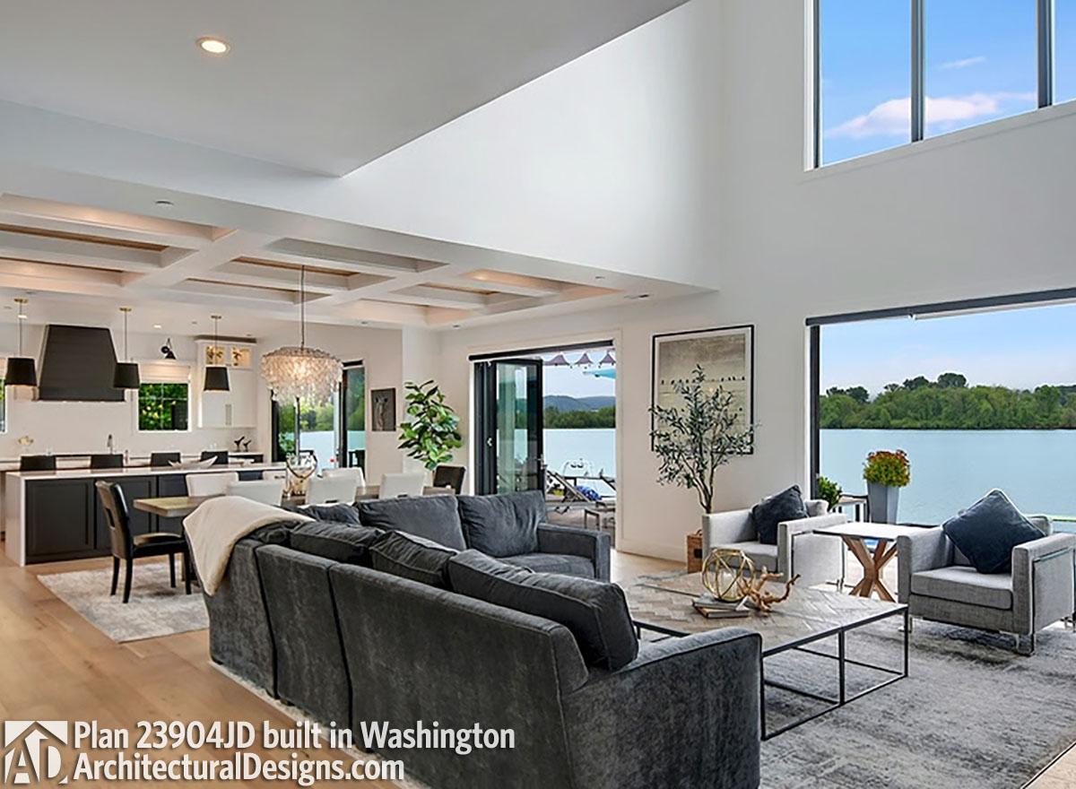 Great room with coffered ceiling, open kitchen, and large windows overlooking a lake.