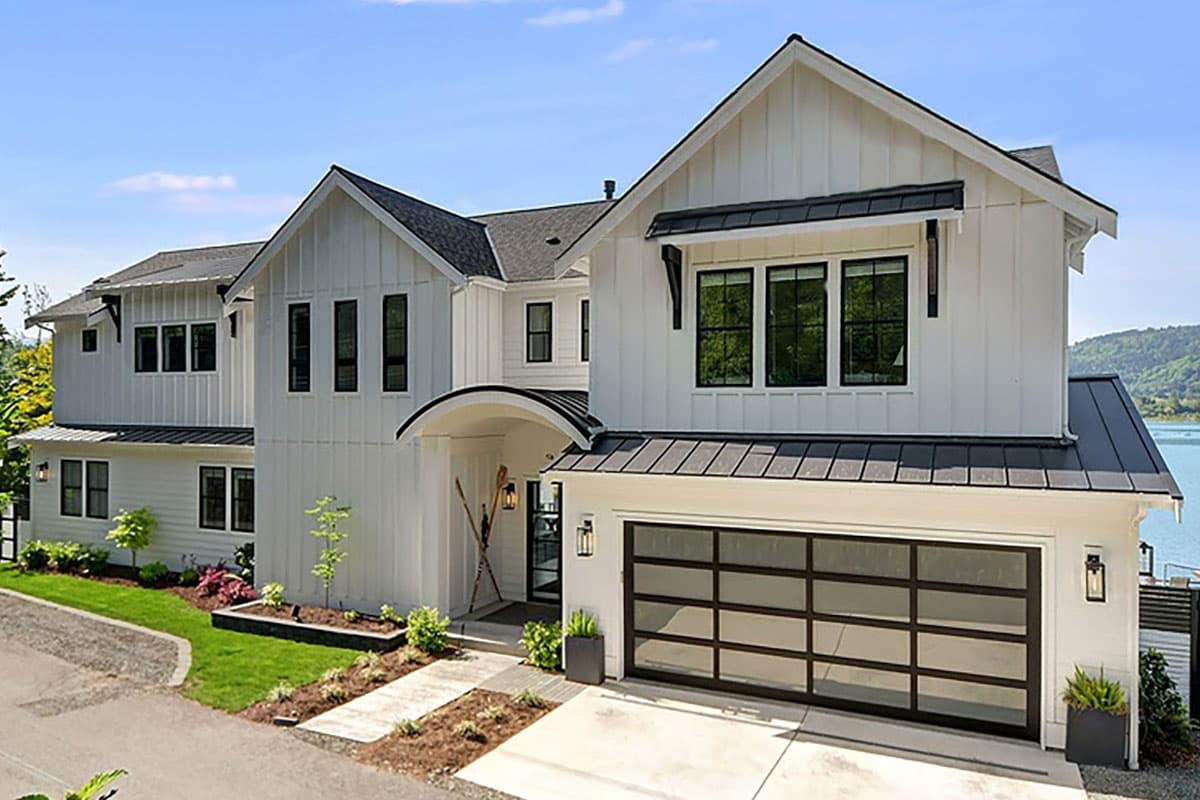 House plan exterior. Modern farmhouse style with board and batten siding, multiple gables, and a glass-paneled garage door with a black metal roof.
