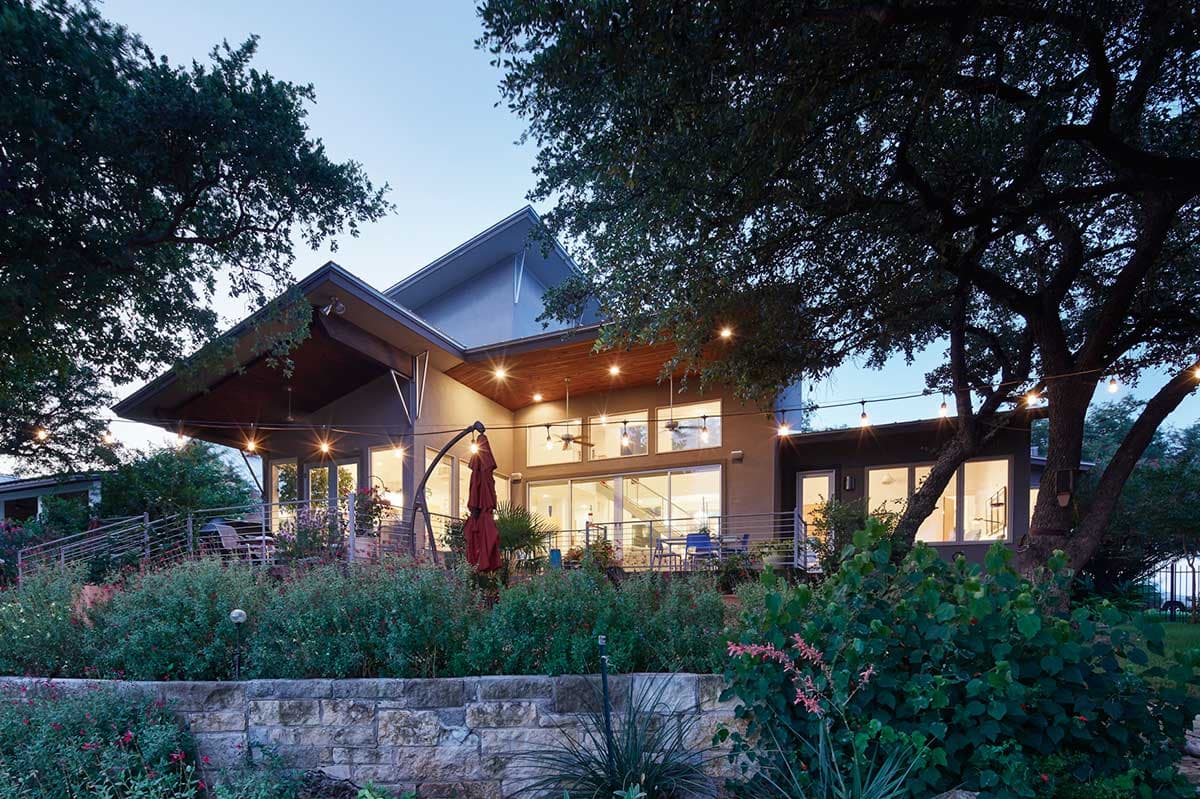 Modern house plan exterior with expansive windows, sloped rooflines, covered patio, and stone retaining wall.