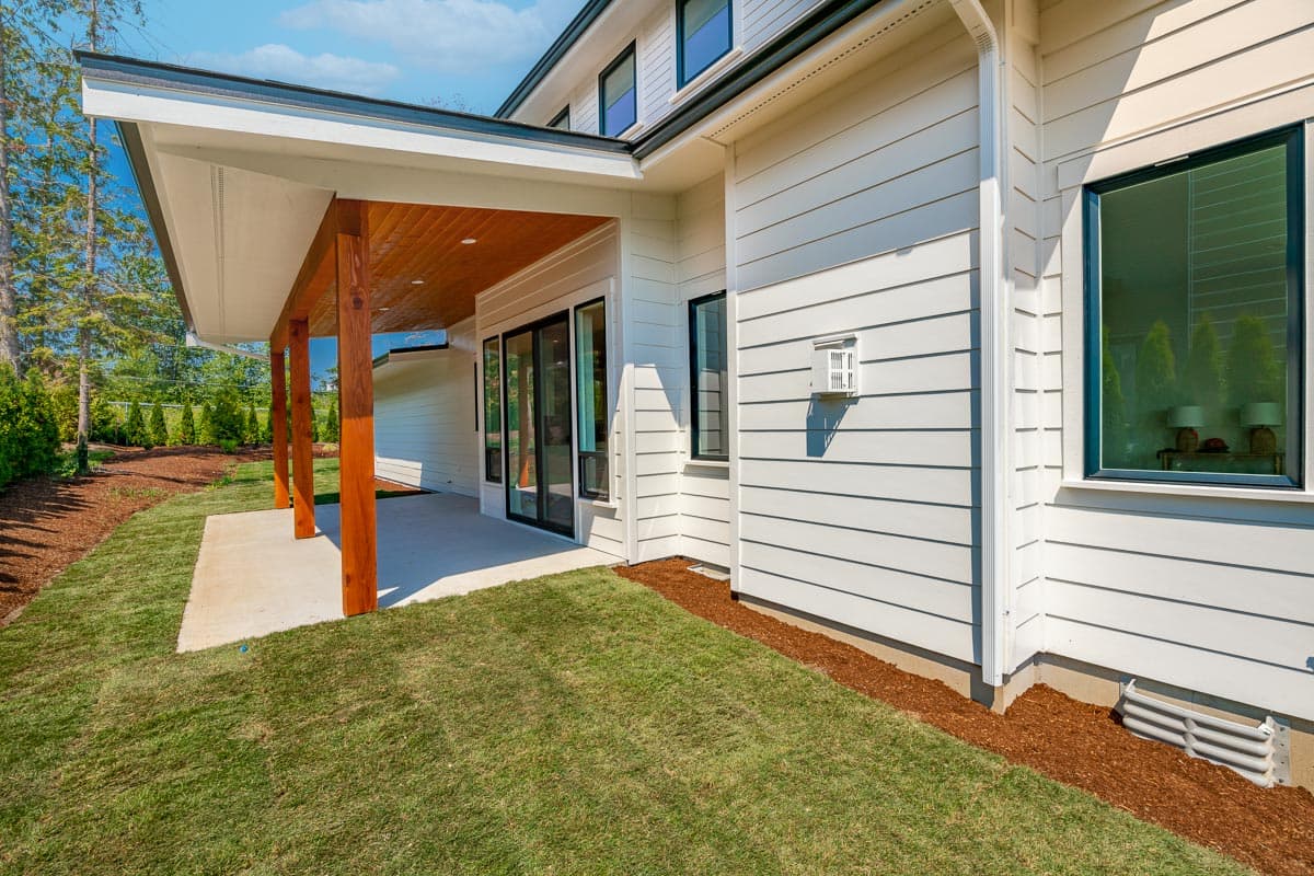 House plan exterior with covered patio, wood-paneled ceiling, exposed beams, and white horizontal siding.