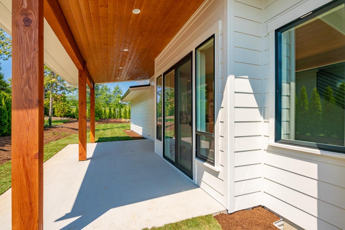 Exterior house plan detail: covered porch with wood ceiling and posts, white lap siding, and large windows.