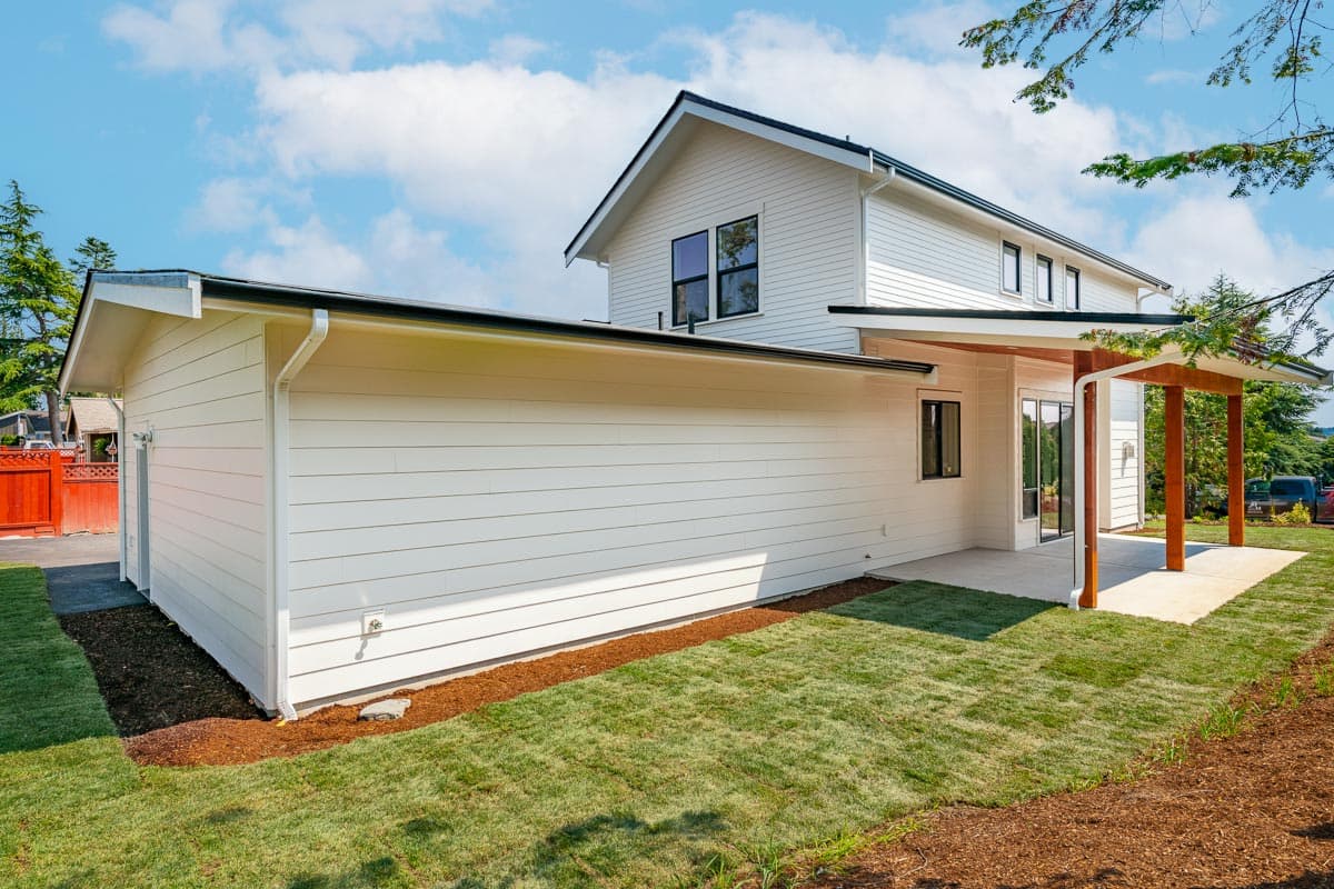 Modern house plan exterior with white lap siding, gable rooflines, attached garage, and covered patio with wood posts.