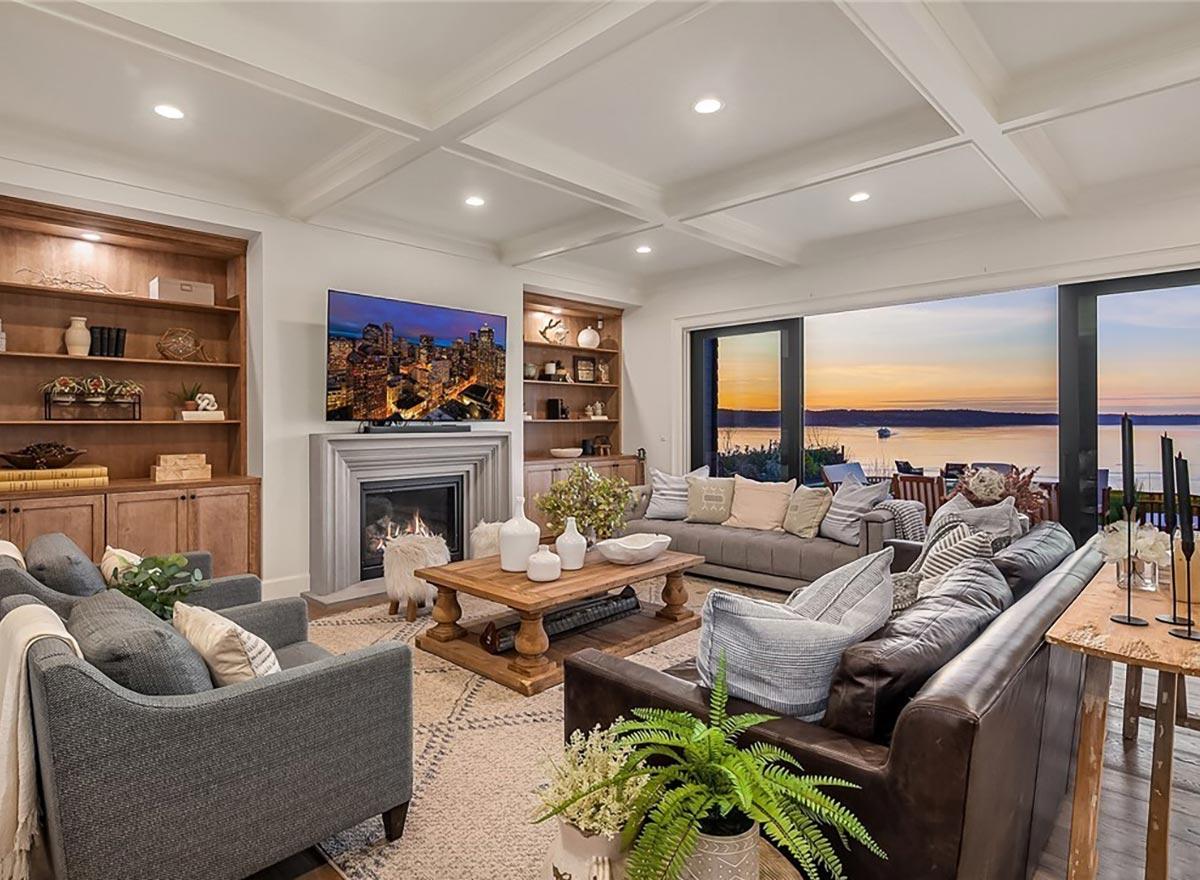 Living room with coffered ceiling, fireplace, built-in shelving, and large sliding doors with water view.