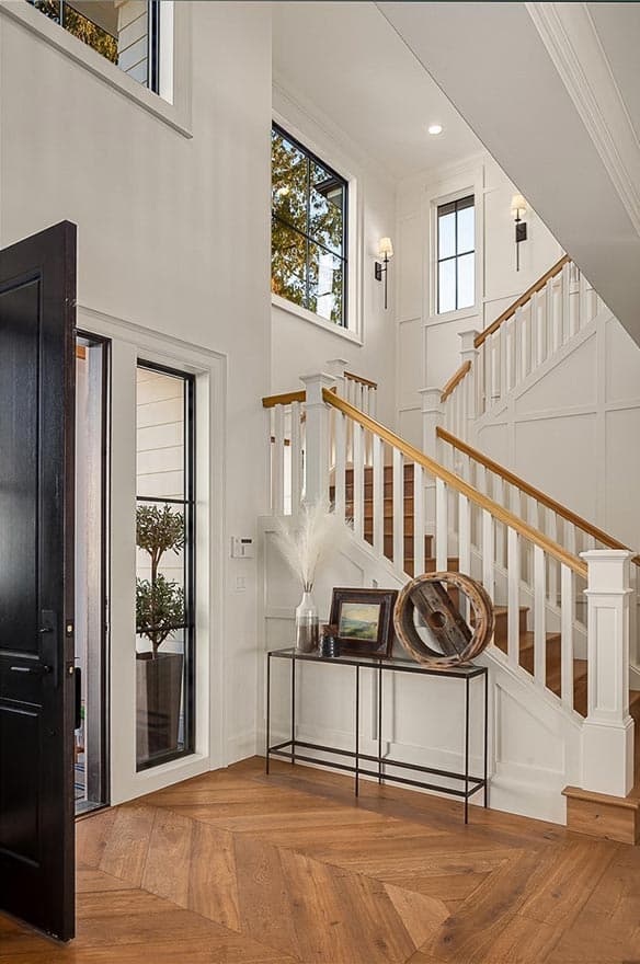Interior view of a grand entryway with a double-height ceiling, staircase, and large windows.
