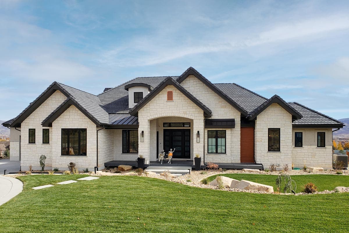 House plan exterior. Two-story, stone facade with multiple gables, a covered entry porch, and a hipped roof. Features include black-framed windows.