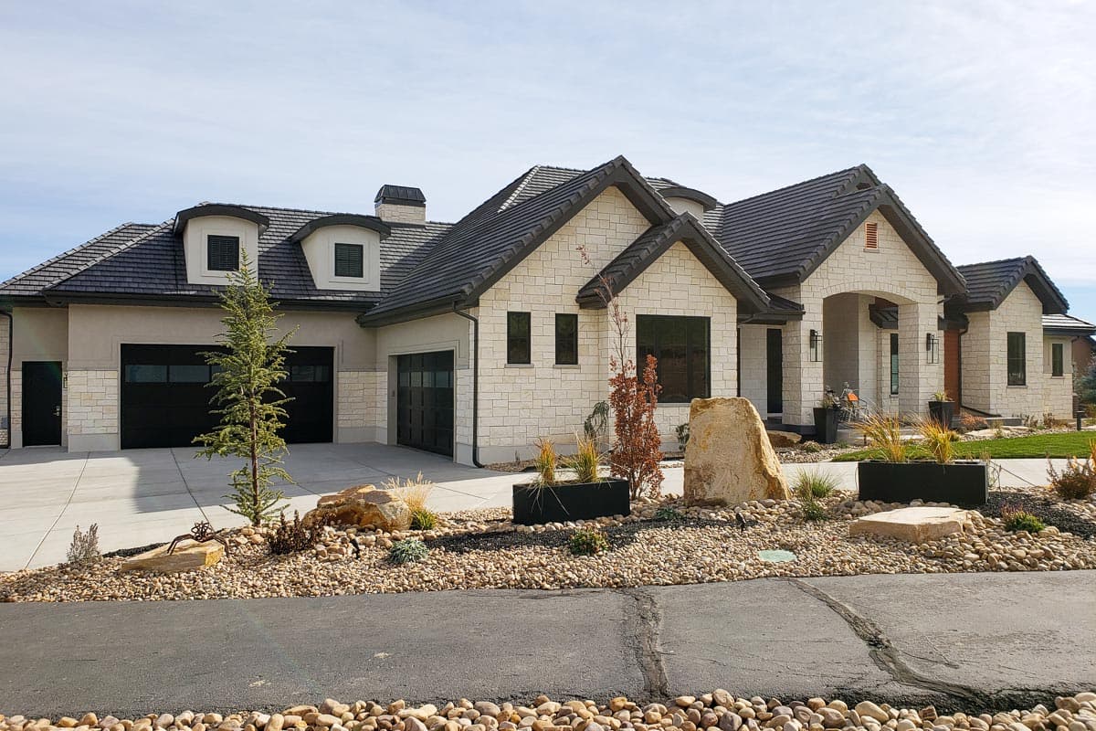 House plan exterior featuring light stone, dark gabled rooflines, dormers, and a three-car garage.