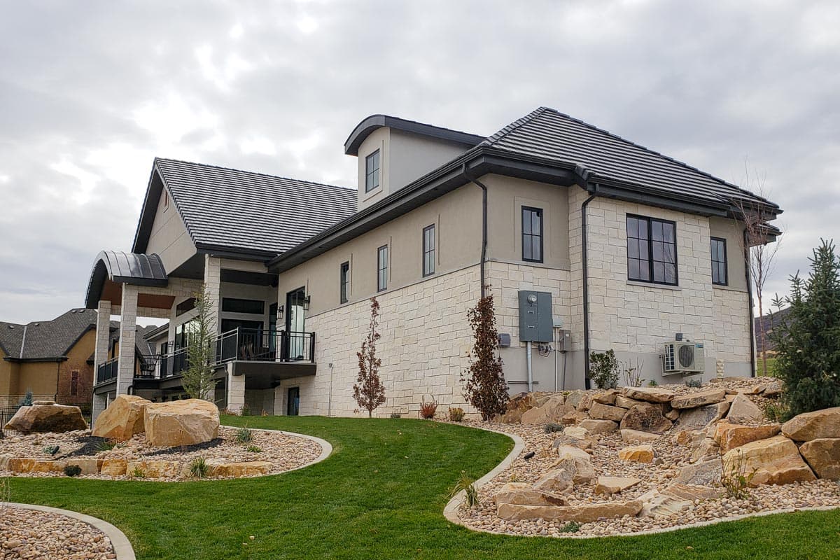 House plan exterior featuring a modern style with stone and stucco facade, multiple gables, covered porch, and balcony.