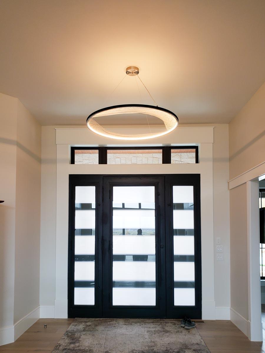 Modern entryway featuring black steel doors with frosted glass panes, clerestory windows, and a circular pendant light.