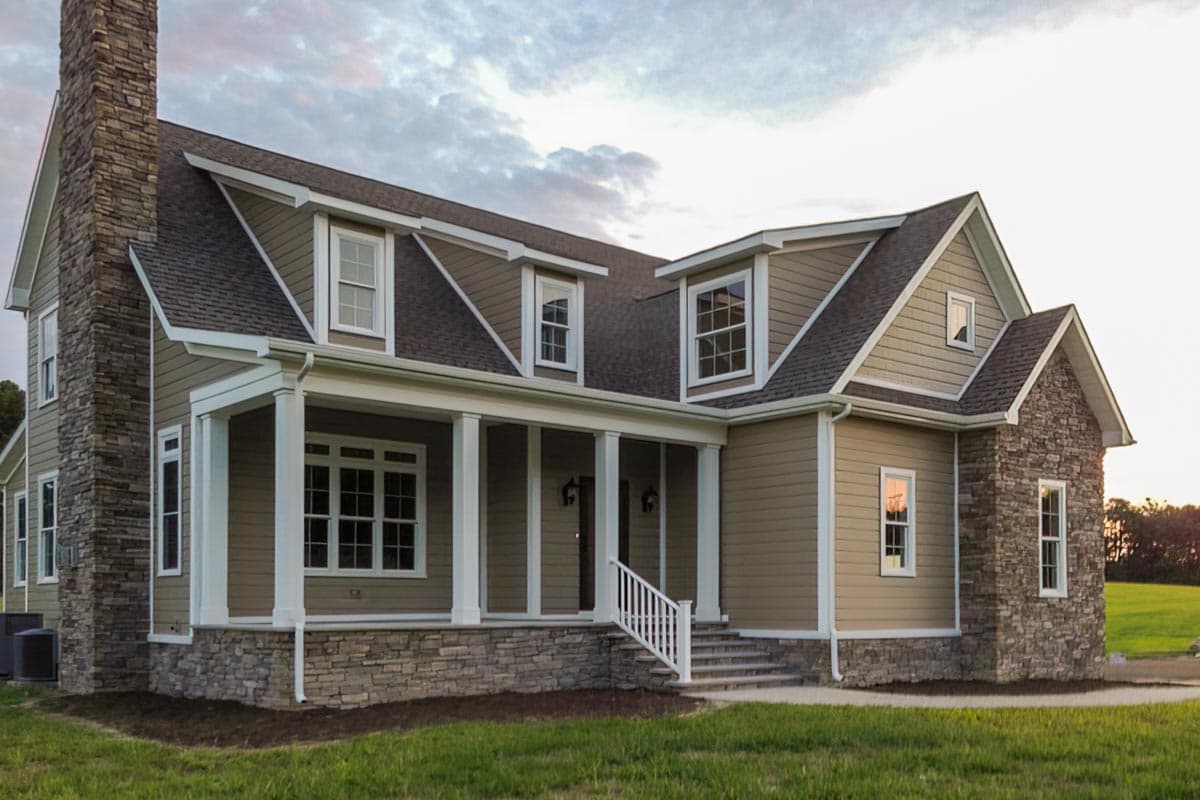 House plan exterior. Two-story home with a stone chimney and foundation. Features a covered porch with pillars and multiple gables.