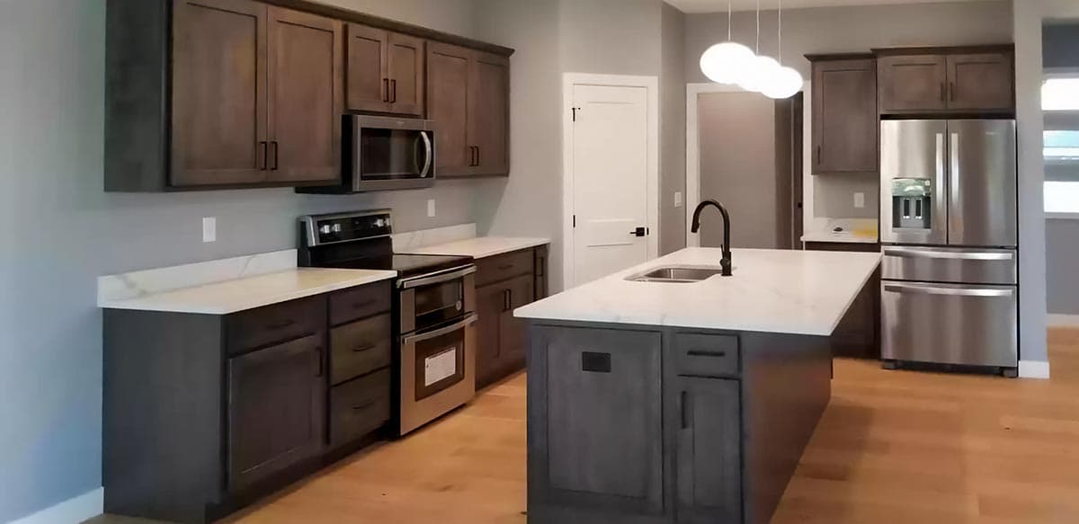 Modern kitchen with dark wood cabinets, white quartz countertops, stainless steel appliances, and a central island with a sink.