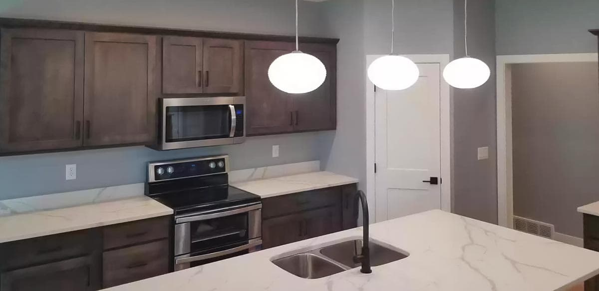 Kitchen featuring dark wood cabinets, stainless steel appliances, white quartz countertops, and pendant lights.
