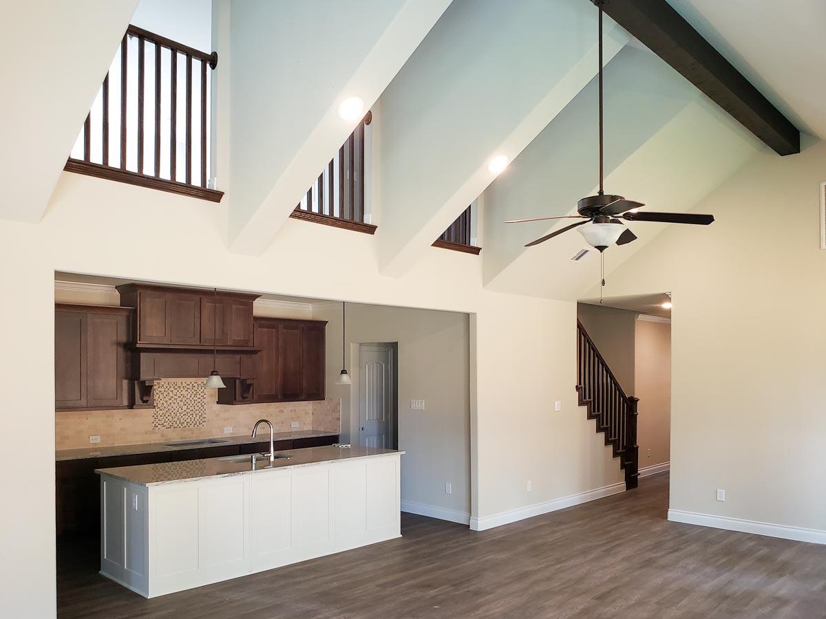 Open concept living area with vaulted ceiling, dark wood beams, kitchen island, and staircase.