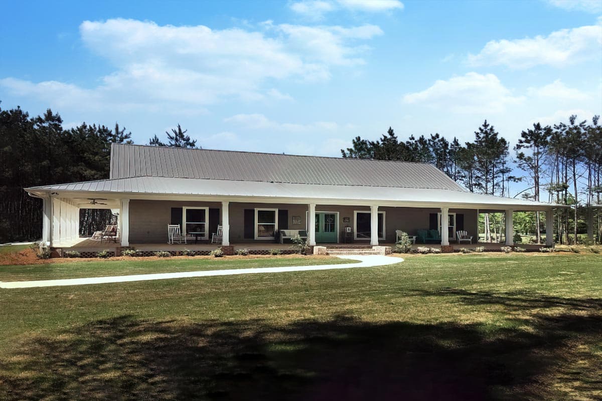 House plan exterior with a Ranch style. Features include a wrap-around porch, metal roof, and rectangular windows with dark shutters.