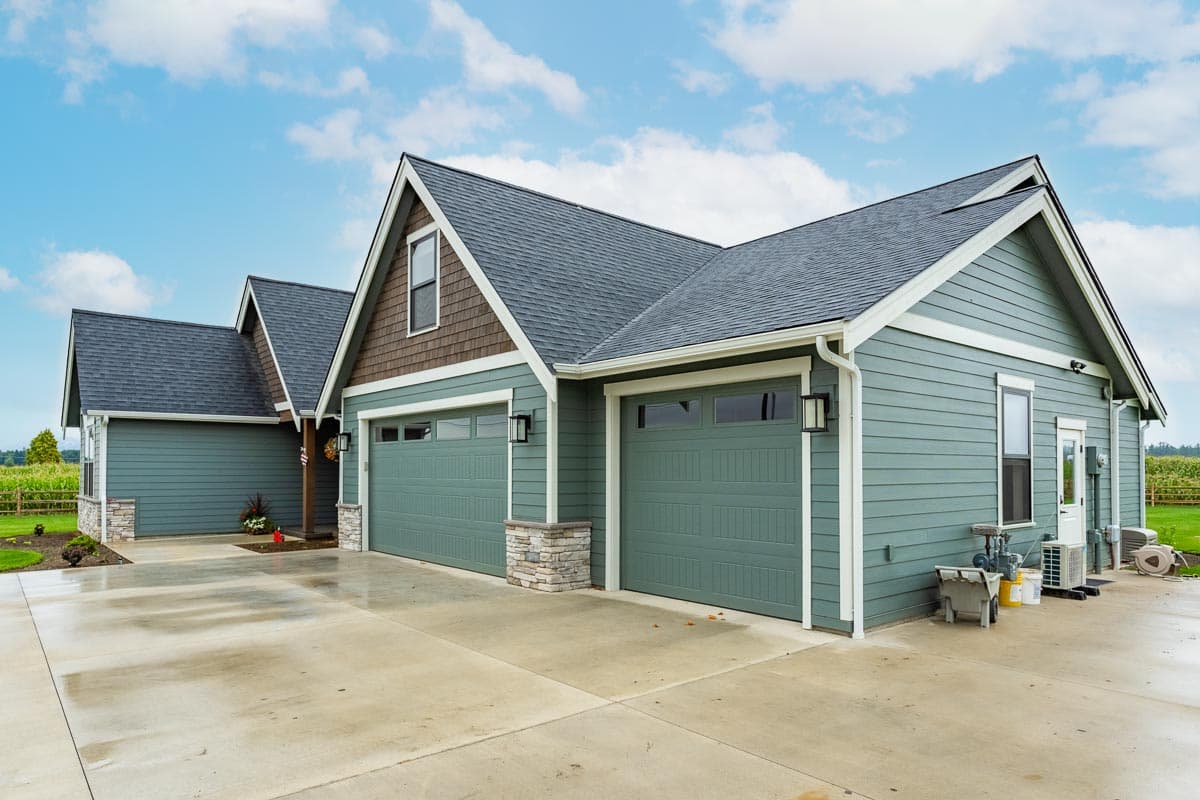 Modern Farmhouse house plan exterior with three garage bays, gabled dormers, stone accents, and horizontal siding.