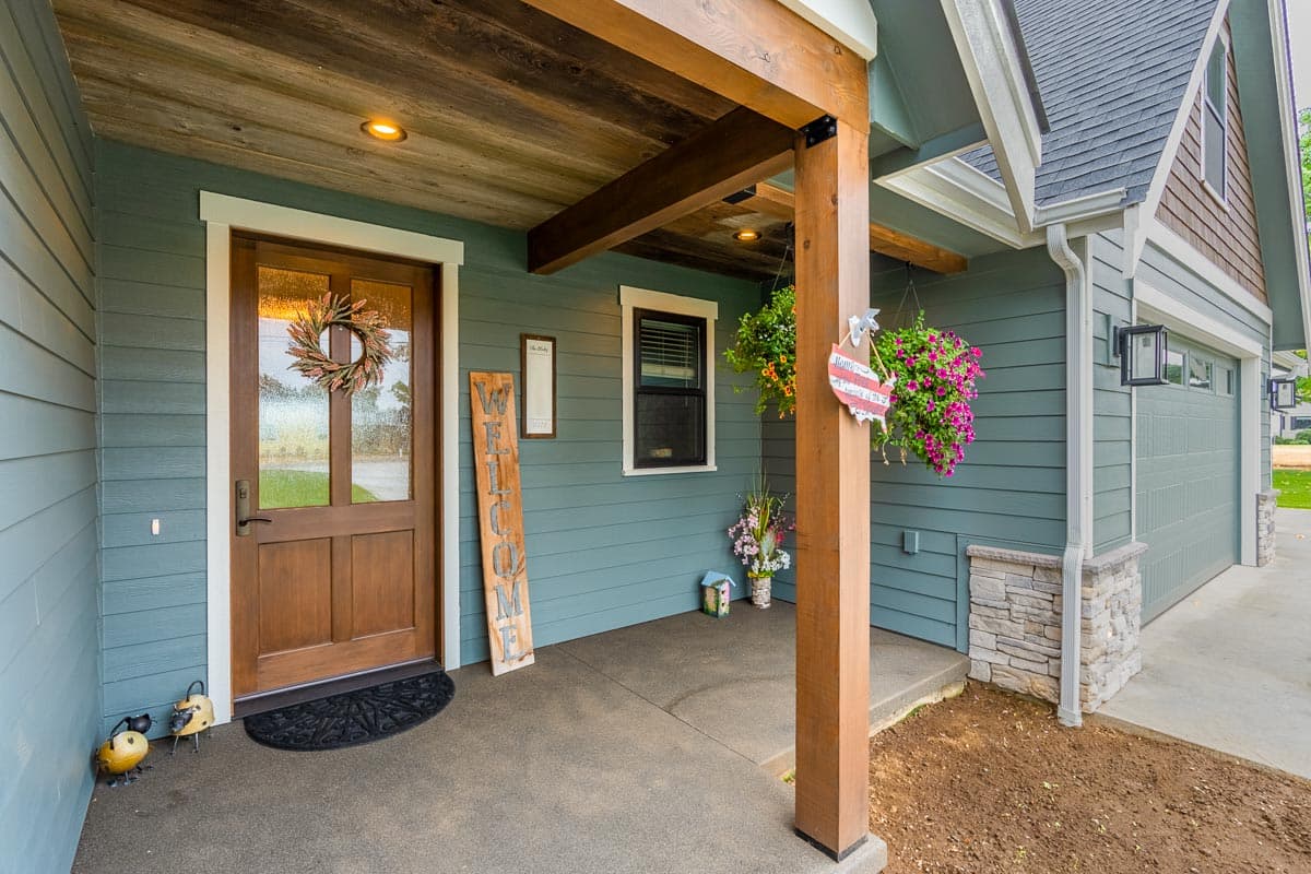 House plan exterior: Covered porch with wood posts, gabled roof, and double garage with stone accents.