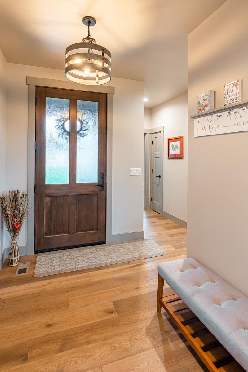 Entryway with glass-paneled wooden door, hanging light fixture, hardwood floors, and bench.