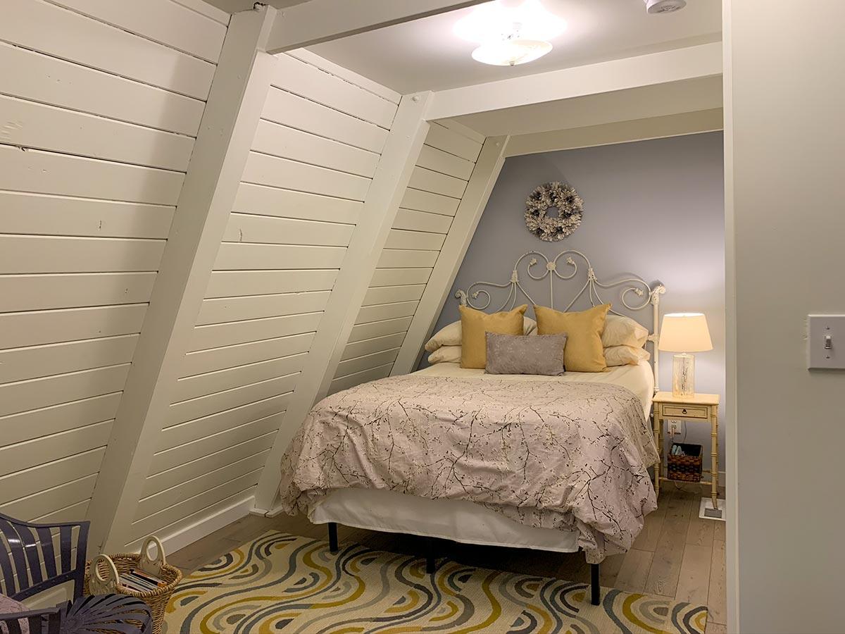 Bedroom interior with a white metal bed, pitched ceiling with exposed beams, and paneled walls.