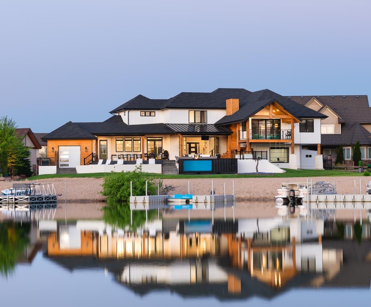 Modern house plan exterior with multiple gables, wood accents, covered patio, and a pool overlooking the water.