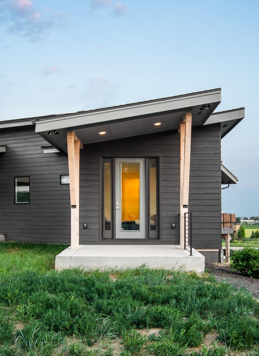 Modern house plan exterior with asymmetric rooflines, wood supports, and dark horizontal siding.