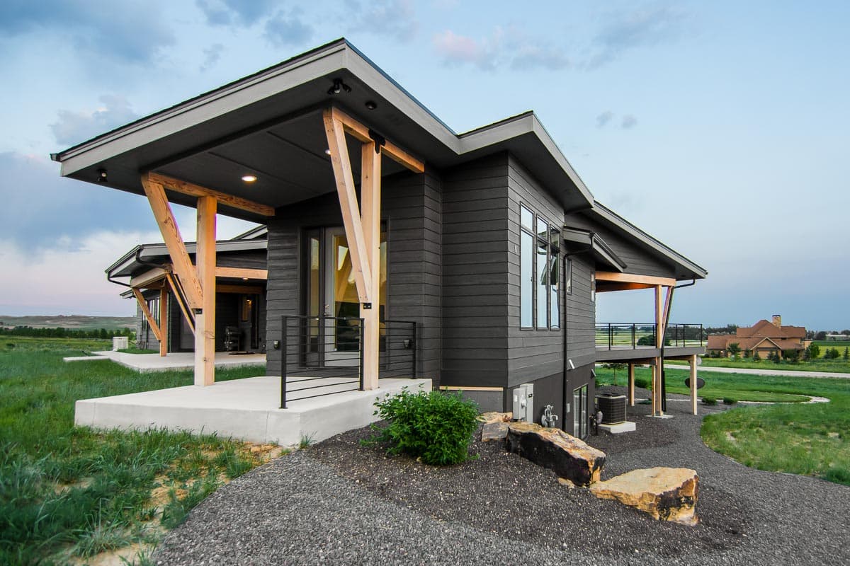 Modern house plan exterior with dark siding, cantilevers, exposed wood beams, and a large covered porch.