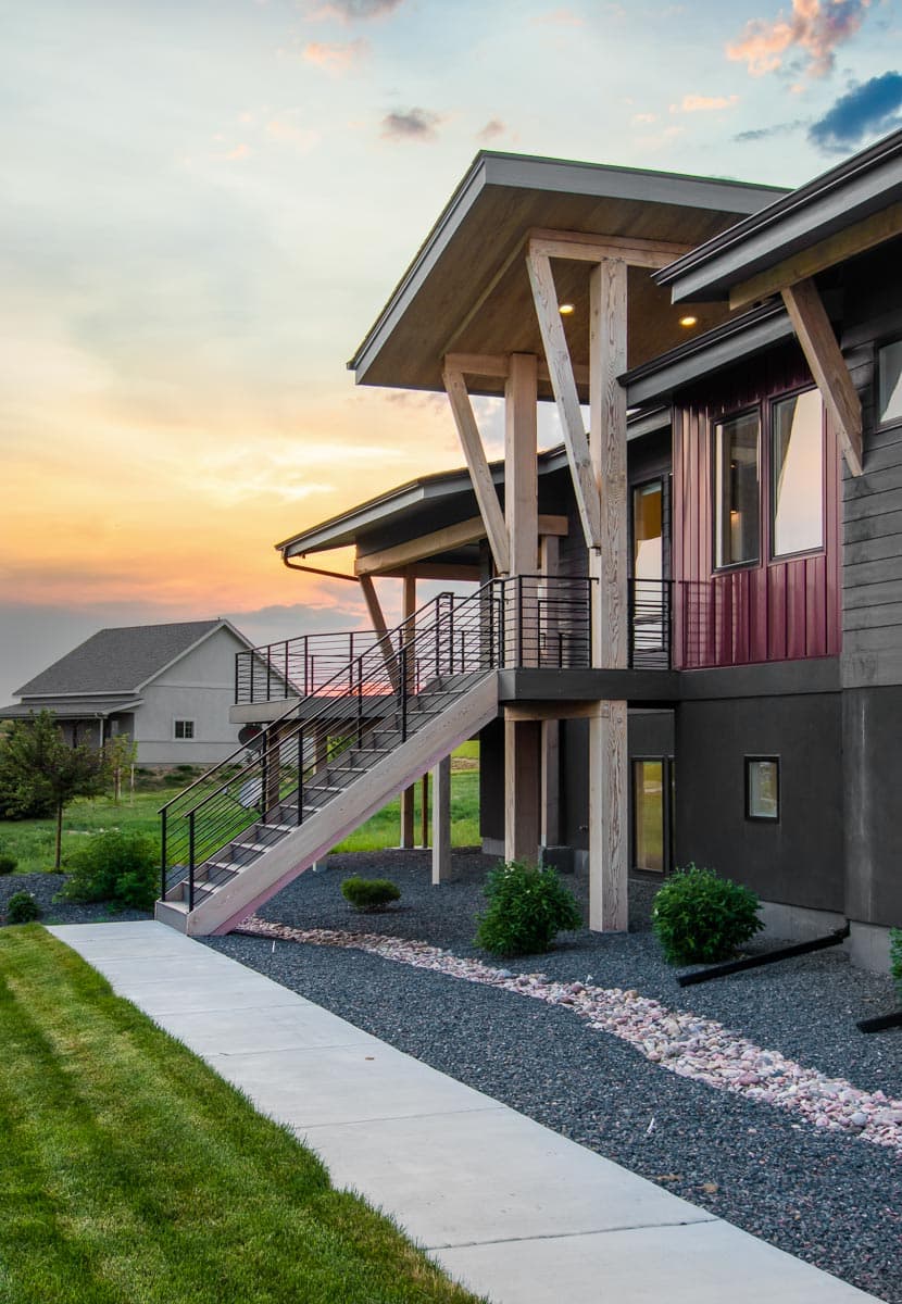 House plan exterior with a modern style, featuring a prominent angled roofline, exposed wood beams, and a split staircase with metal railings.