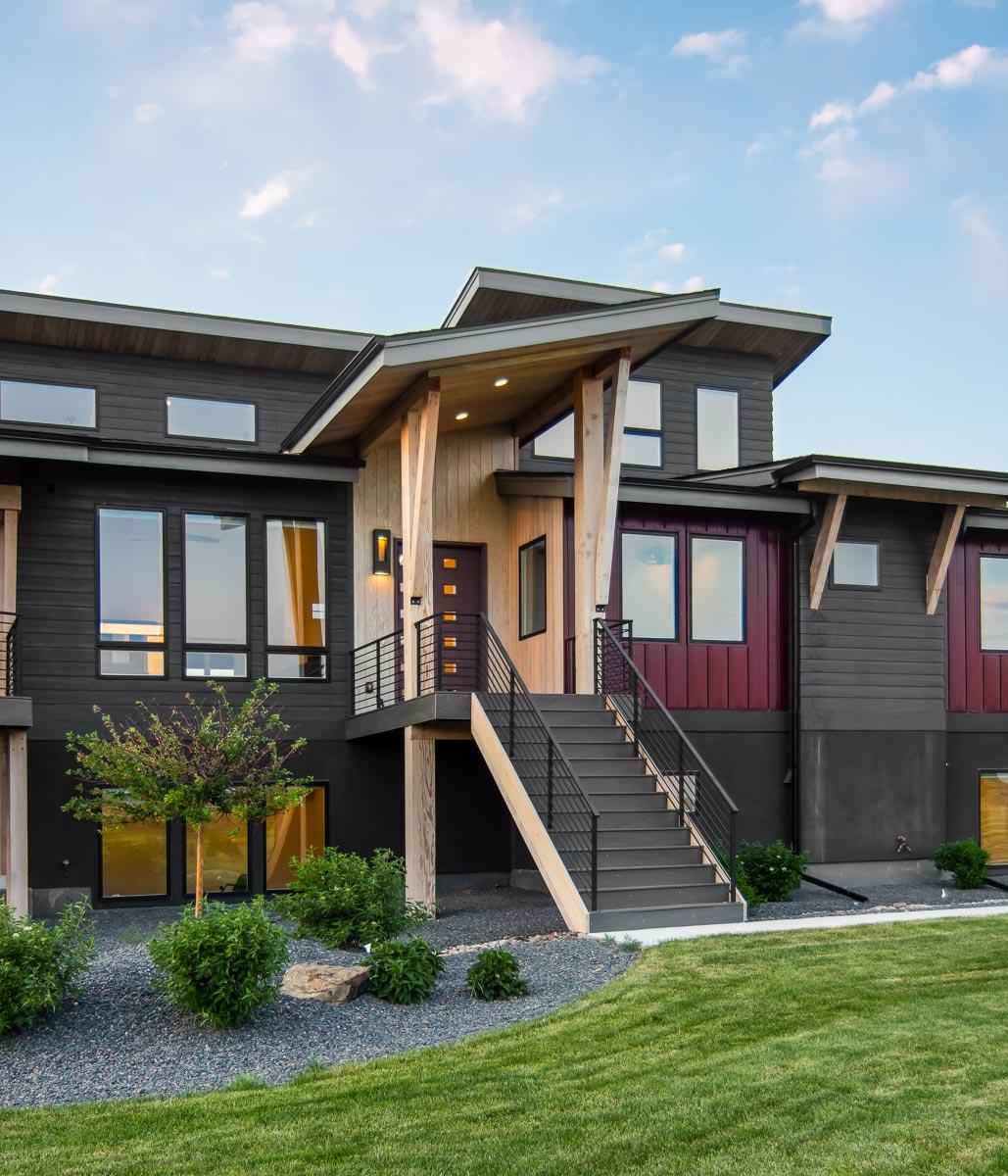 Modern house plan exterior with steeply pitched rooflines, dark siding, wood accents, and prominent elevated stairs.