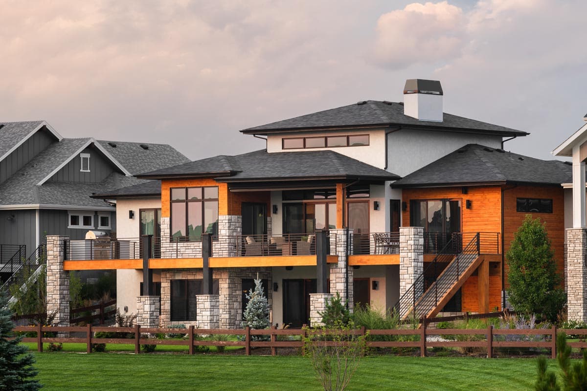 Modern house plan exterior with stacked stone, wood siding, multiple balconies, and a prominent chimney.