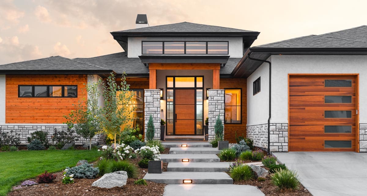 Modern house exterior with wood siding, stone accents, large wood garage door with windows, and expansive entryway.