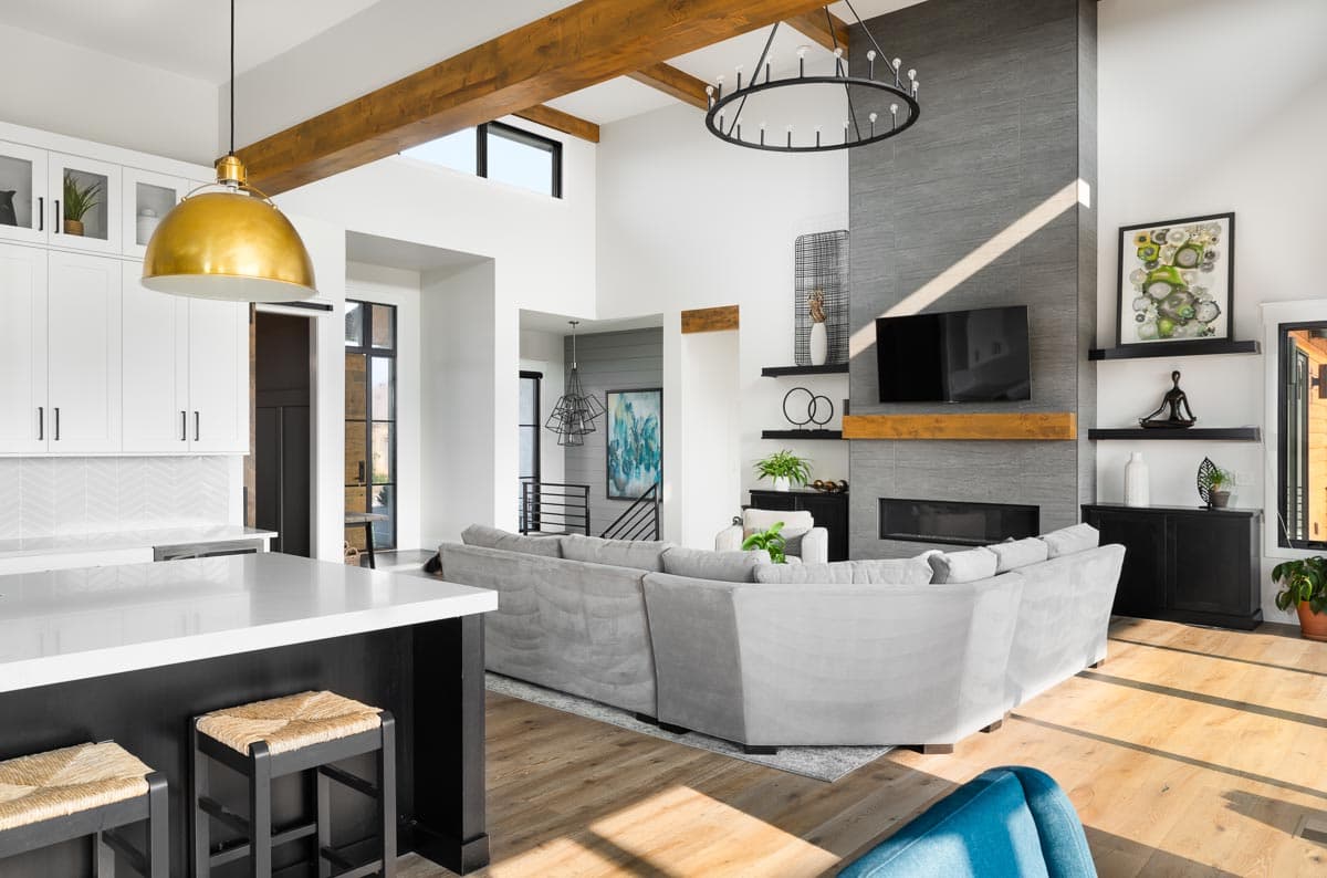 Open-concept living area with vaulted ceilings, wood beams, large stone fireplace, and kitchen island with seating.
