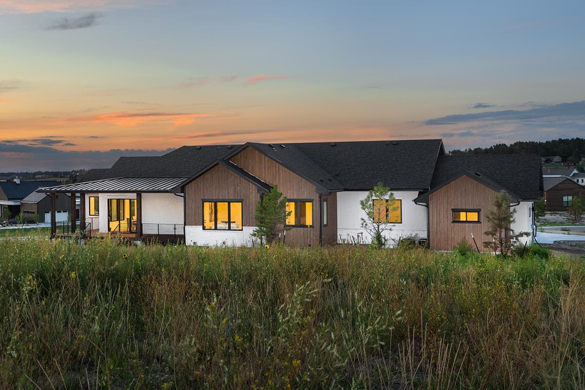 Modern ranch house plan exterior with a covered porch, white stucco, wood siding, gables, and dark roof.