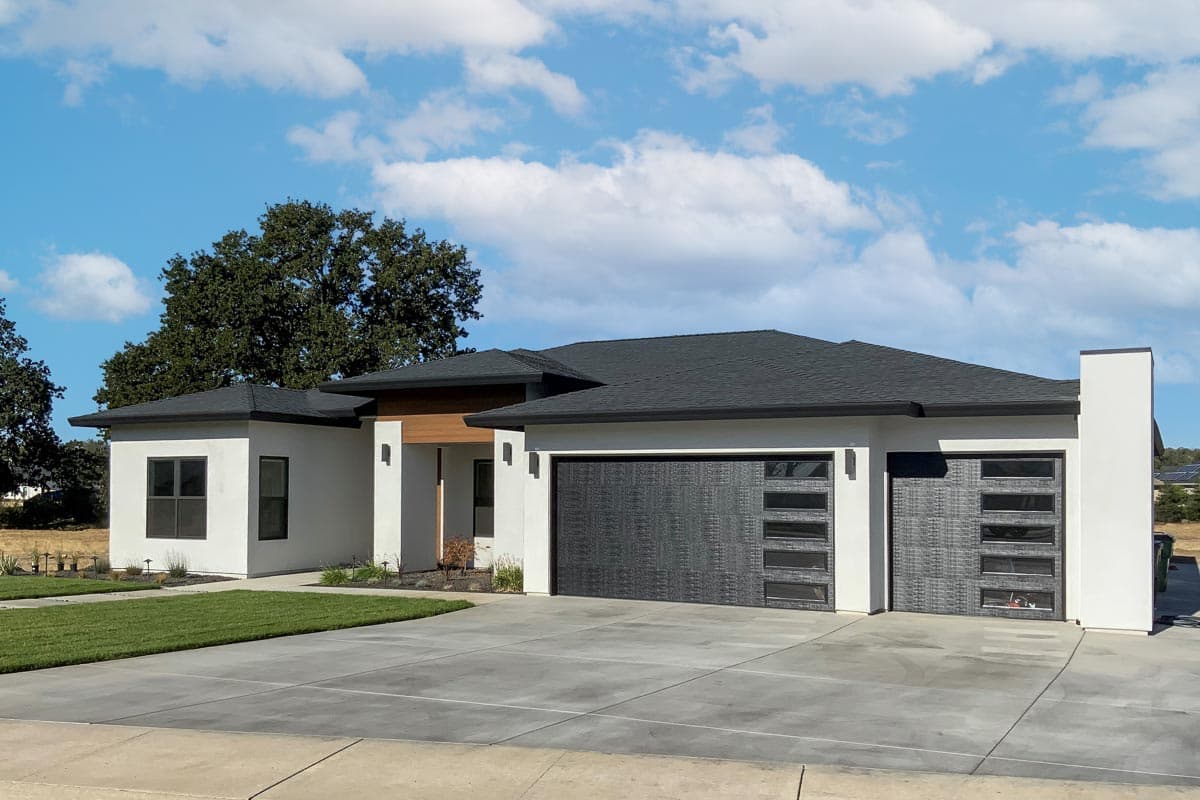 Modern single-story house plan exterior with a flat roof, stucco finish, and two dark wood garage doors with glass panels.