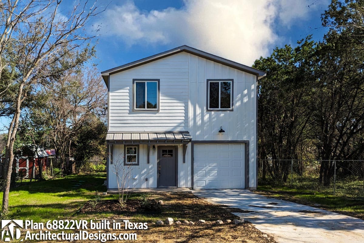House plan exterior, two stories, white horizontal siding, metal awning over entry, single-car garage.