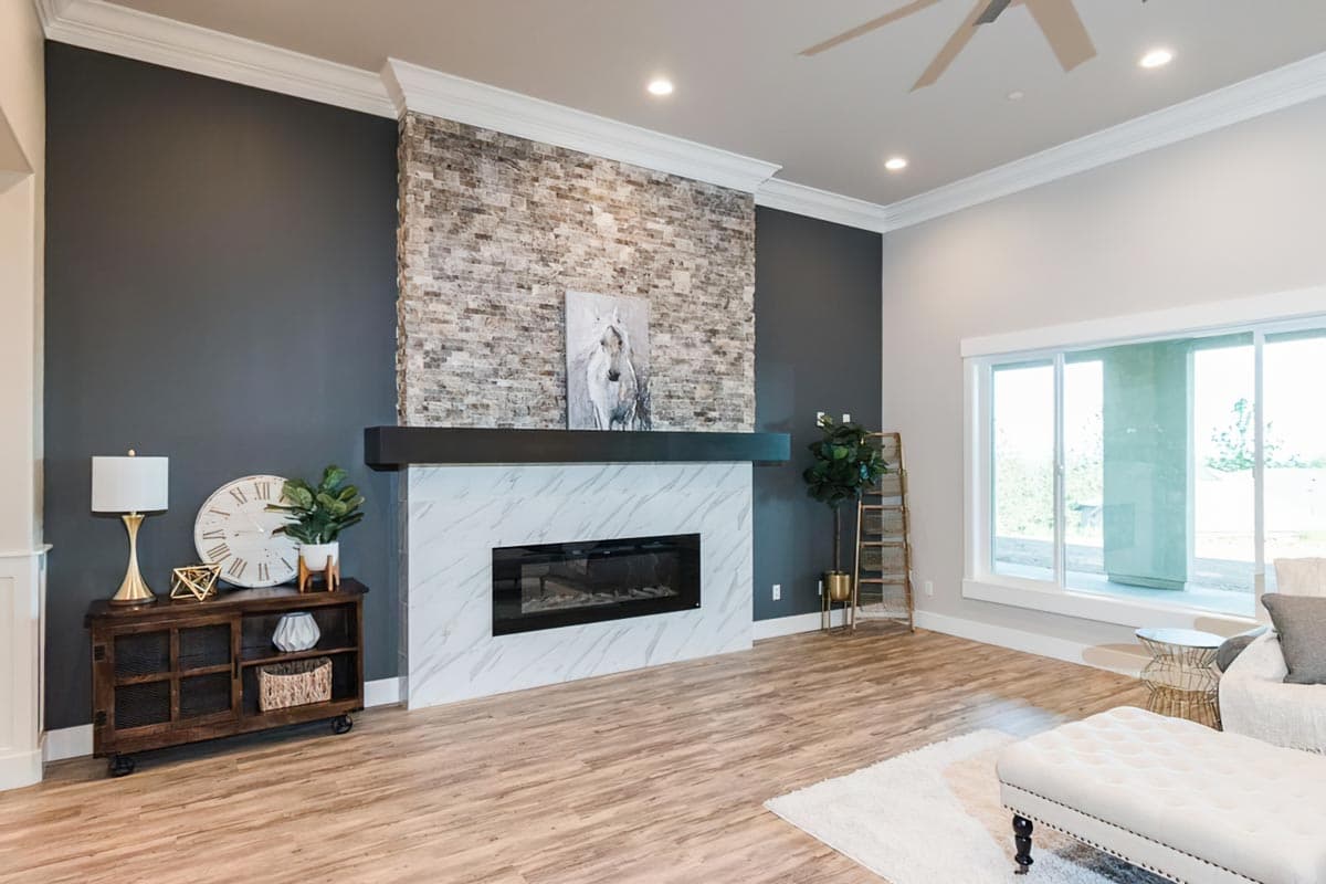 Living room interior with stacked stone and marble fireplace, large windows, and a vaulted ceiling with a fan.