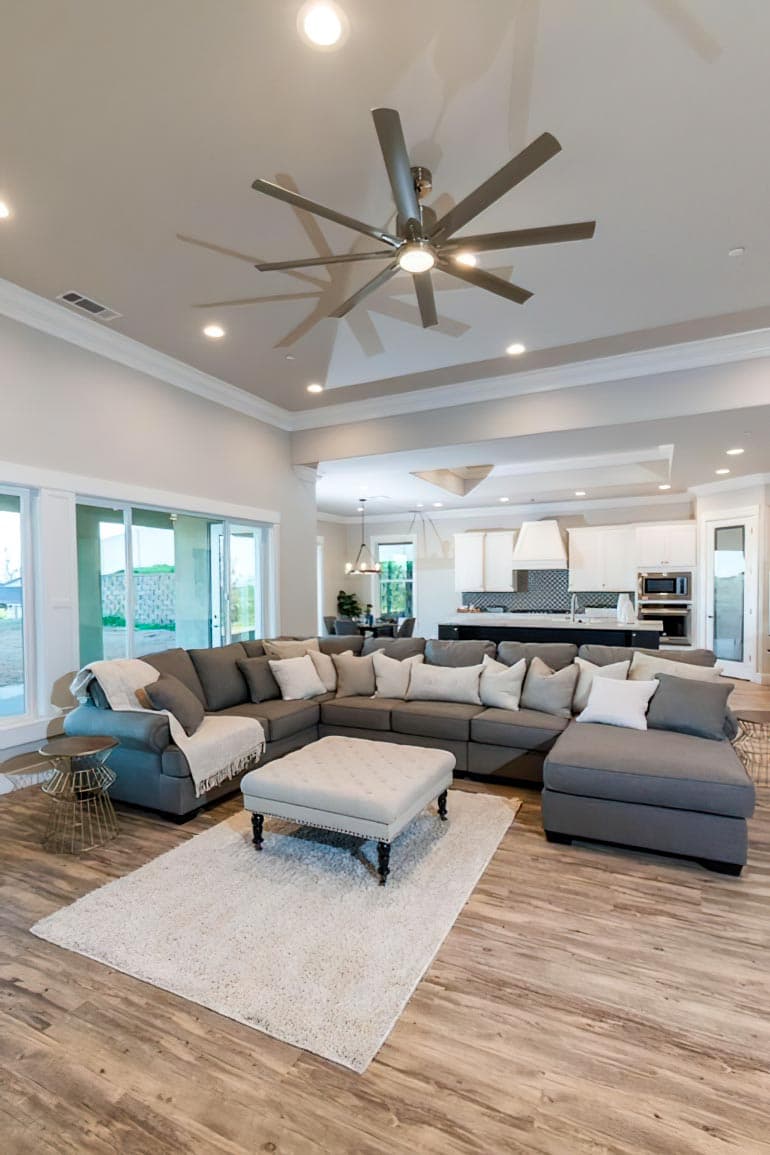 Open-concept living area with large sectional sofa, ottoman, and adjacent kitchen with island and modern backsplash.