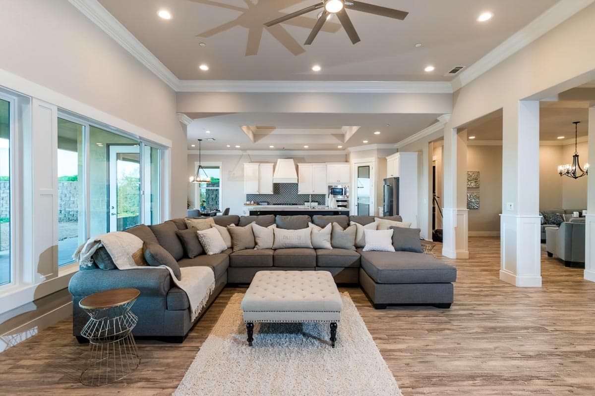 Open-concept living area with sectional sofa facing kitchen. Features large windows, coffered ceiling, and island.