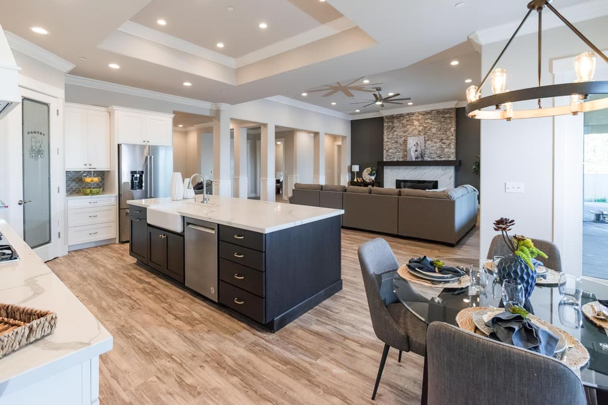 Open-concept living area with kitchen island, dining space, and living room featuring stone fireplace.