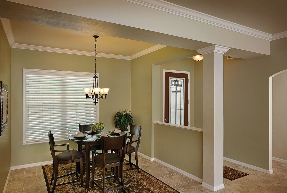 Dining area with glass-top table, four chairs, chandelier, and frosted window. Open doorway to hall visible.