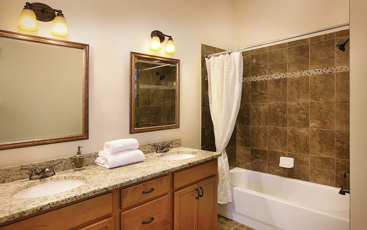 Bathroom with double vanity, granite countertop, wood cabinets, and tiled shower with curtain.