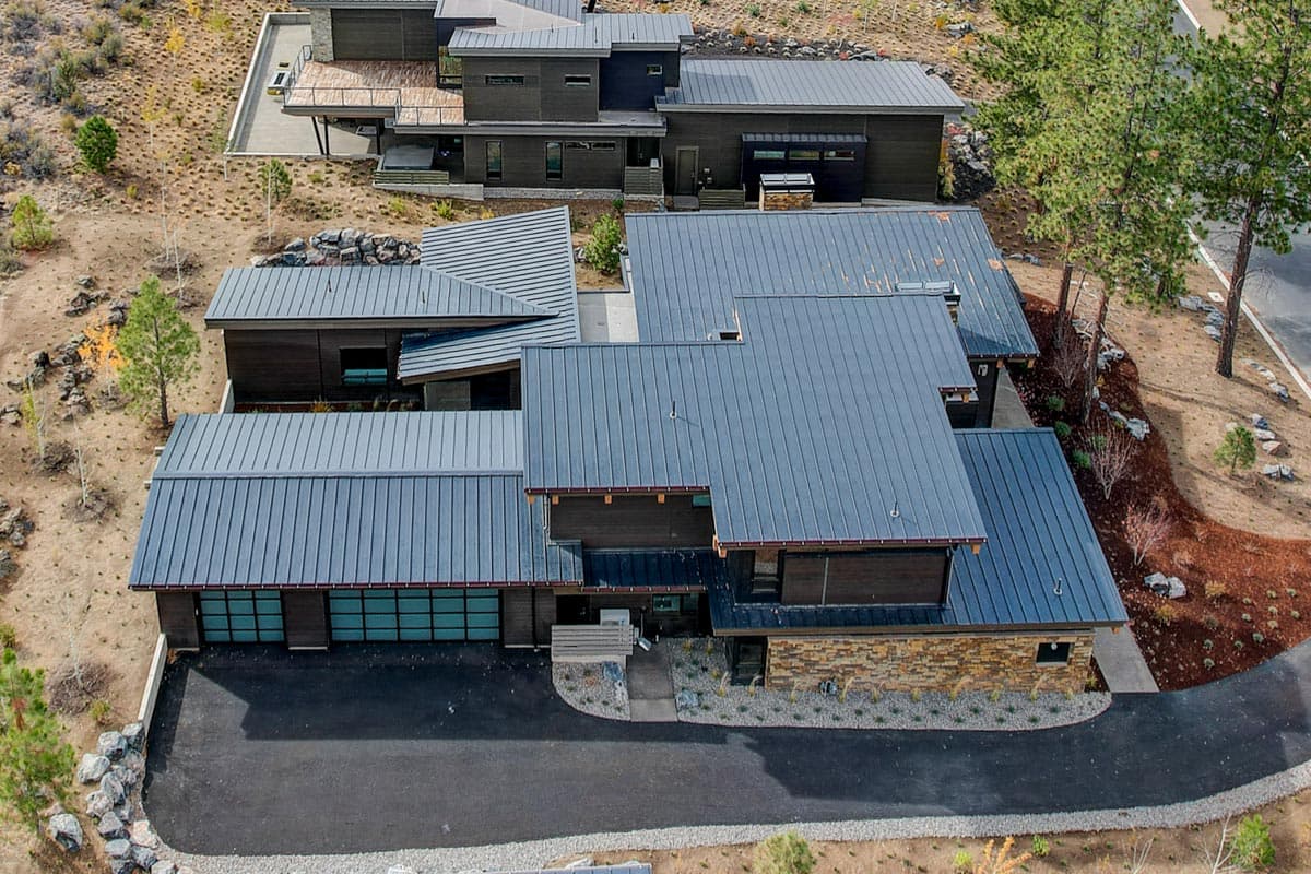 Modern house plan exterior with dark wood siding, stone accents, and multiple gabled metal rooflines.