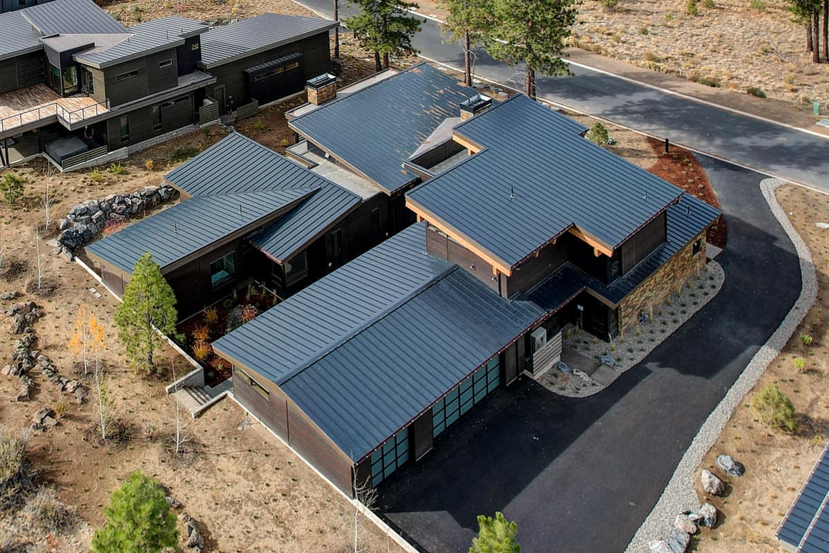 Modern house plan exterior with dark wood siding, stone accents, dark metal roofs, and attached garage.