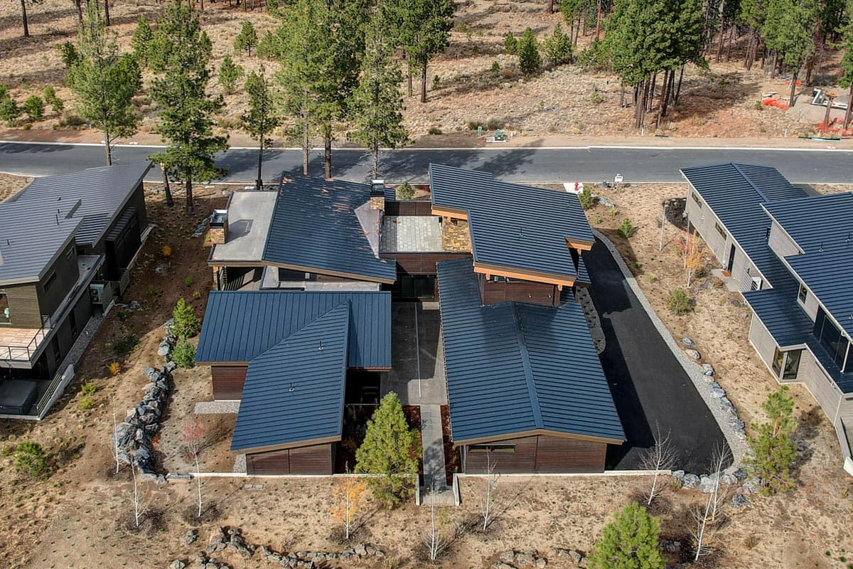Modern house plan exterior with multiple dark metal sloped roof sections, wood siding, and courtyards.