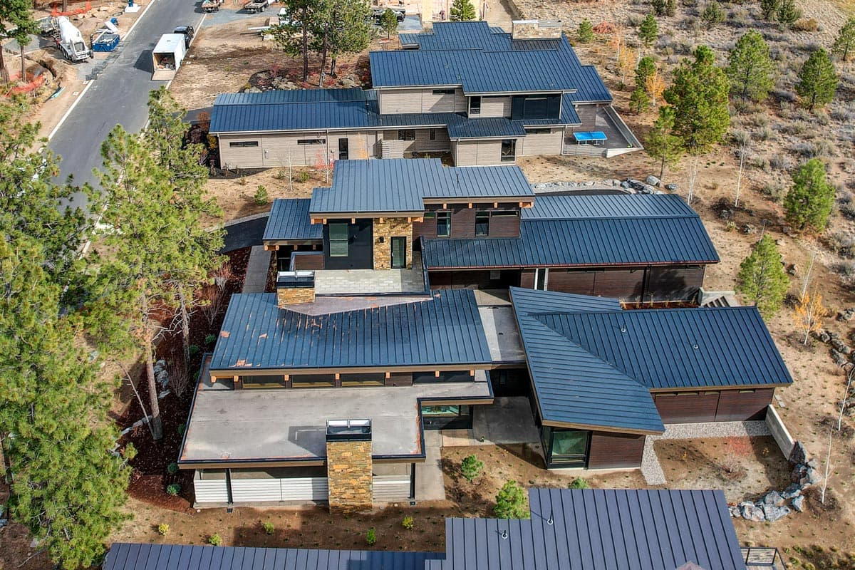 Modern house plan exterior with multiple gabled roofs, stone chimney accents, and extensive dark metal roofing.